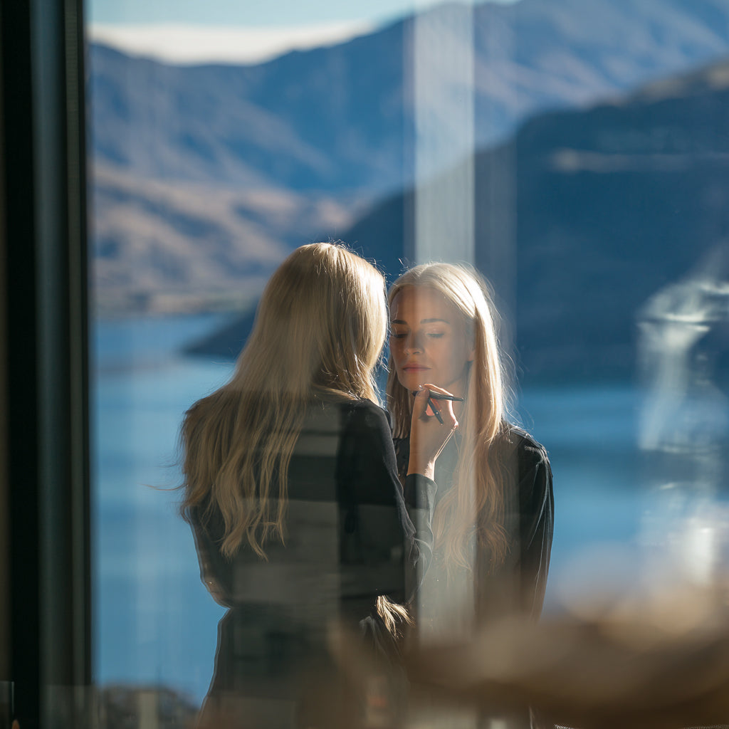Luxury bridal makeup application in Queenstown New Zealand, soft glam bride preparation with flawless light-diffused complexion and alpine lake view